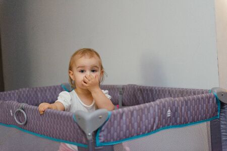 Little baby in a cot. Portrait child baby close up. 18 month old baby girl stands in the crib.の写真素材