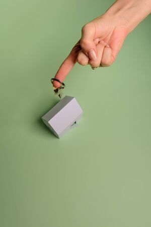 White family paper house. House keys in hand on mint background paper. Minimalistic and simple concept, style. Copy space. Vertical orientation. Family moving or removal concept.の写真素材