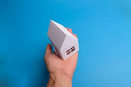 White family paper house over block of flats on blue background paper. Minimalistic and simple concept, style. Copy space. Vertical orientation.の写真素材