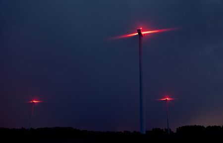 Wind turbines on a dramatic dark blue clouds in the sky. Storm ahead is coming. Red warning light on the windmillの写真素材