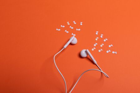 white earphones and white paper notes on orange background. view from aboveの写真素材