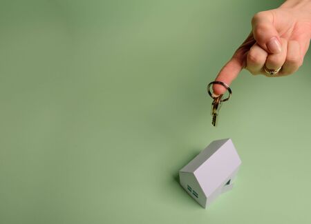 White family paper house. House keys in hand on mint background paper. Minimalistic and simple concept, style. Copy space. Vertical orientation. Family moving or removal concept.の写真素材