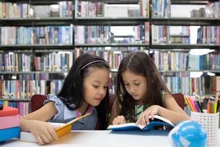 Couple asian school girl kid concentrate reading book together in education library.の写真素材