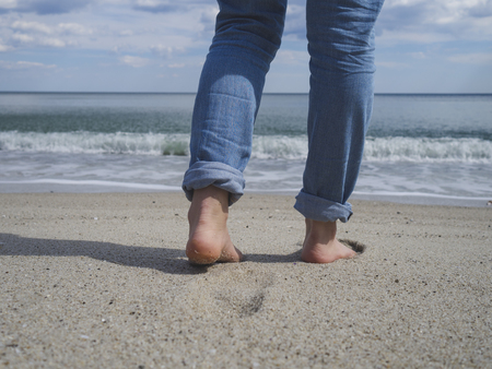 Womans bare feet walking on a beautiful sandy beach towards the water