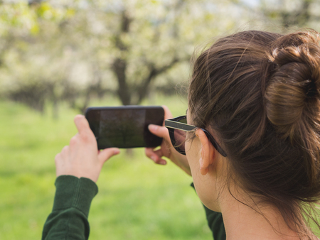 Young woman taking a picture of the view while hiking in a national park with a smart phoneの写真素材