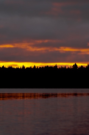 Orange sunrise shot from the surface of a lake with the silhouette of a forestの写真素材