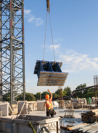 Construction worker receiving a stack of scaffolding pieces from a crane on a construction siteの写真素材