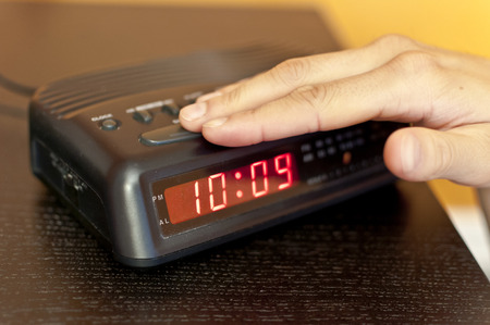 Hand pressing the snooze button on a digital alarm clockの写真素材