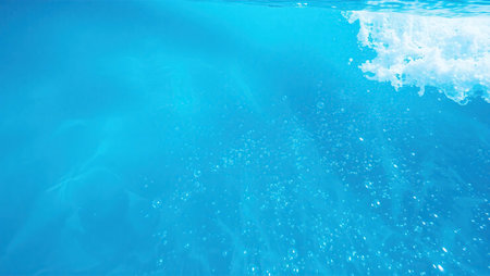 An abstract underwater shot of shimmering blue water with a cascade of bubbles and bright light breaking the surface.の素材