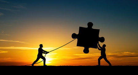 Two silhouetted figures work together to move a large puzzle piece against a vibrant sunset, symbolizing unity, problem-solving, and shared effort towards a common objective.の素材