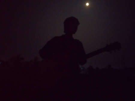 A boy with guitar in a moonlit nightの写真素材