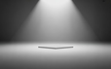 The a minimalist product setup featuring a small white square surface illuminated by focused lighting against a dark background. The lighting creates a gradient effect, with bright light at the center gradually fading into shadows. The overall composition is clean and modern, emphasizing simplicity and contrast.の素材