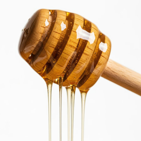 A close-up image of a wooden honey dipper with golden honey dripping from it, set against a plain white background.の素材