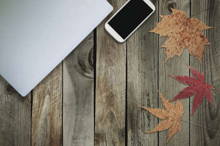 Top View of Work Space on Wooden Table with Laptop, Mobile Phone and Autumn Leaves