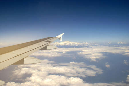 Wing of an Airplane Flying above the Cloud with View of Mount Everest Background, Travelling Conceptの写真素材
