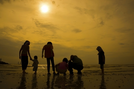 Group of kids playing at the beach during sunset in silhouette の写真素材