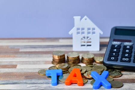 Close up of TAX word on wooden home and stack money coins on the backrgound.の写真素材