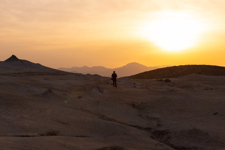 A photographer with a camera takes pictures of mud volcanoes at sunset.の写真素材