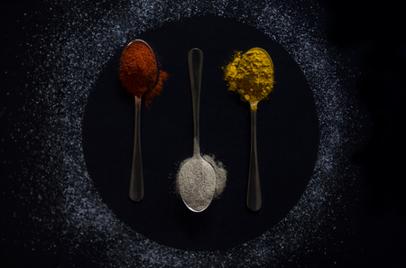 Variety of spices and herbs on kitchen table. Various colorful spices on spoon on black table inside circular form. Pepper, turmeric, powder, salt.の写真素材