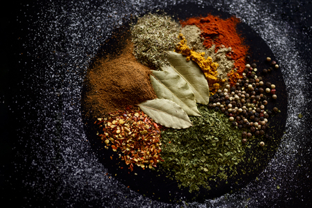 Variety of spices and herbs on kitchen table. Various colorful spices on black table inside circular form. Pepper, turmeric, powder, cinnamon, leaf, salt.の写真素材