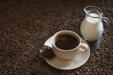 Coffee cup full of coffee on plate with cookies and roasted coffee beans around the cup on wooden tableの写真素材