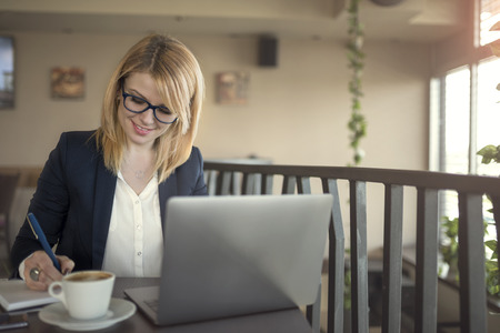 Business woman is working on computer, taking notes, thinking about something in a coffee shop, restaurant.の写真素材