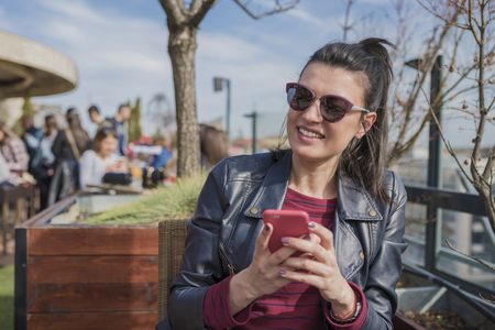 Beautiful smiling young woman sitting outdoors and chatting on mobile phone. Girls time, enjoying, lifestyle.の写真素材
