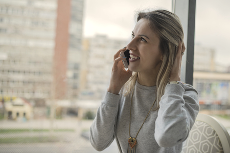Beautiful smiling young woman sitting indoors and talking on mobile phone. Girls time, enjoying, lifestyle.の写真素材