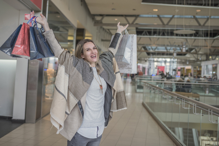 Smiling girl with Shopping Bags in Shopping Mall. Fashion Shopping Girl Portrait. Beauty Woman with Shopping Bags in Shopping Mall. Shopper. Sales. Shopping Centerの写真素材