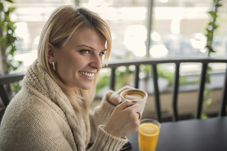 Portrait of young woman drinking cup of coffee and enjoying her leisure time. Business woman drinking coffee in cafe during her work break. Enjoying the moment and delicious sip of coffee.の写真素材