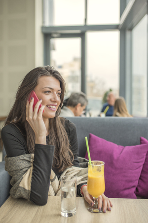 Portrait of young beautiful women using mobile phone at coffee shop. Young female enjoying in a restaurant laughing, talking and gossiping on her mobile phone.の写真素材