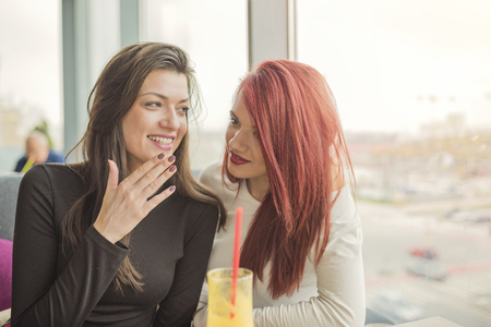 Portrait of two young beautiful women at coffee shop, girl talk. Two female friends enjoying together in a restaurant laughing, talking and gossiping.の写真素材