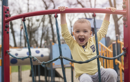 Adorable little boy having fun on playground. Active sport leisure for kids outdoor in park. Little boy with blue eyes in yellow shirt playing and having fun on playground.の写真素材