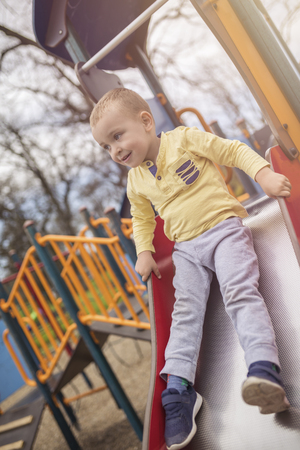 Adorable little boy having fun on playground. Active sport leisure for kids outdoor in park. Little boy with blue eyes in yellow shirt playing and having fun on playground.の写真素材