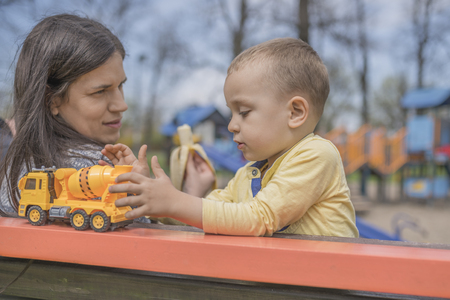 Closeup portrait of a happy mother and son playing on playground and having fun. Young mother playing with her baby outside in park. Mom and son.の写真素材