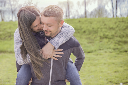 Beautiful young couple enjoying piggyback in sunny day and smiling while playing outdoorsの写真素材