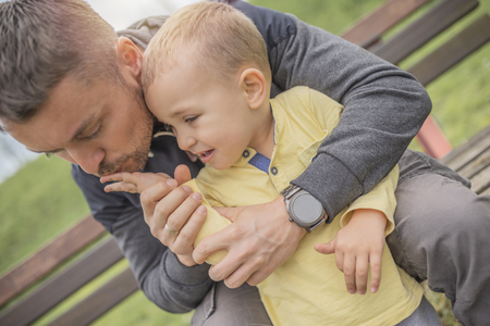 Closeup portrait of a young father and crying kid on playground. Young father hugs crying child. Dad and son.の写真素材