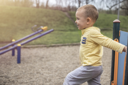 Adorable little boy playing on playground on sunny day. Activity for kids in park. Cute boy with blue eyes in yellow shirt enjoying on playground.の写真素材
