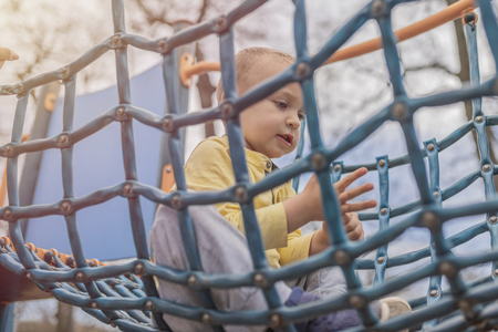 Adorable little boy having fun on playground. Active sport leisure for kids outdoor in park. Cute Little boy with blue eyes in yellow shirt playing in park, in nature. Kids and play.の写真素材