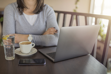 Young girl with gray sweater drinking coffee and using laptop in restaurant, taking break from studying. Drinking coffee and looking for information on internet.の写真素材