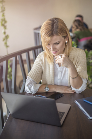 Young business woman using her laptop computer to solve business problems. Pretty woman using computer in restaurant. Blonde attractive girl is working in coffee shop. の写真素材