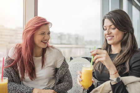 Portrait of two young beautiful girls. Two young female friends enjoying together in a restaurant laughing, talking and gossiping.の写真素材