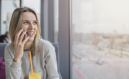 Beautiful smiling girl sitting and talking on mobile phone in coffee shop, restaurant. Girls time, enjoying in sunny day.の写真素材