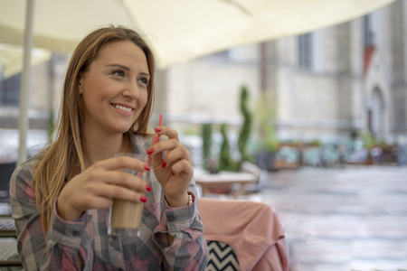 Charming young girl having fun in coffee shop. Pretty caucasian female relaxing in cafe during free time on sunny day. Girl drinking coffee in restaurant.の写真素材