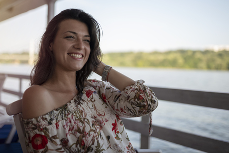 Portrait of beautiful young girl on sunny day in nature, near river. Cheerful woman model sitting in cafe enjoying free time. Pretty girl having fun outdoor.の写真素材