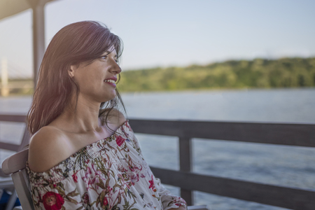 Portrait of beautiful young girl on sunny day in nature, near river. Cheerful woman model sitting in cafe enjoying free time. Pretty girl having fun outdoor.の写真素材