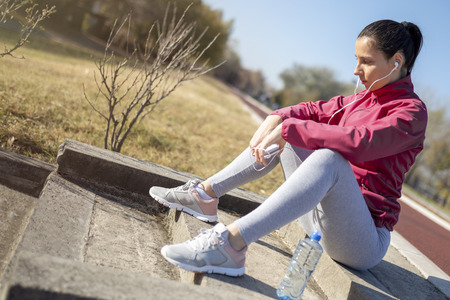 Beautiful fitness girl taking a break outside from workout. Running woman. Female Runner preparing for jogging and listening to music.の写真素材