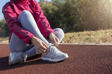 Young fitness woman runner athlete. Girl  jogger training and doing workout outdoors in city. Female hands tying shoelace on running shoes before training. Runner getting ready for training.の写真素材