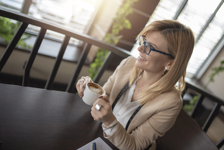 Portrait of young gorgeous female drinking cup of coffee and enjoying her leisure time. Business woman drinking coffee in caffee shop during her work break. Enjoying the moment and delicious sip of coffee.の写真素材