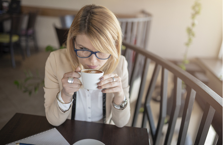Portrait of young gorgeous female drinking cup of coffee and enjoying her leisure time. Business woman drinking coffee in caffee shop during her work break. Enjoying the moment and delicious sip of coffee.の写真素材